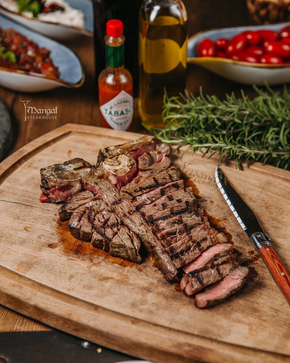 Sliced aged T-bone steak carved on a wooden board with rosemary and olive oil at Mangal Steak House in Baku