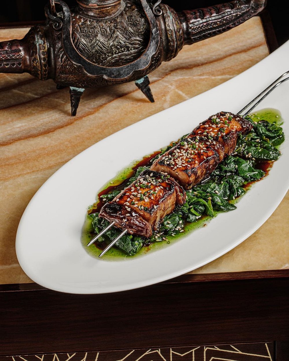 A glazed lamb skewer with sesame over wilted greens, plated at Shur Jazz Hall in Baku