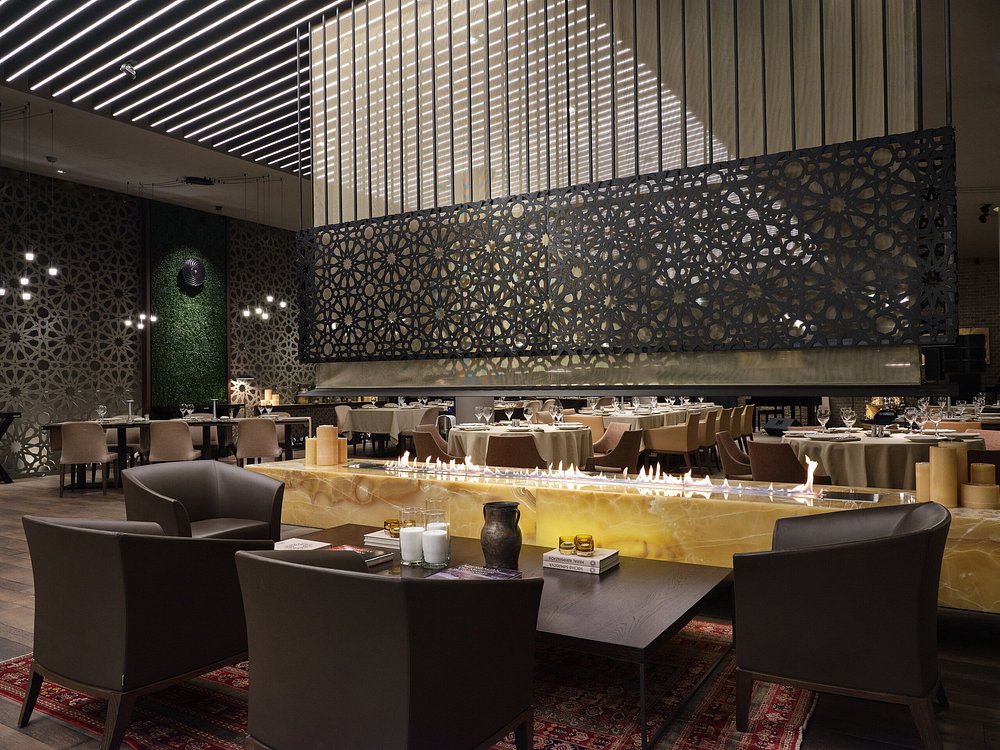A contemporary Baku dining hall with a long onyx fire table, geometric latticework screens and low leather armchairs