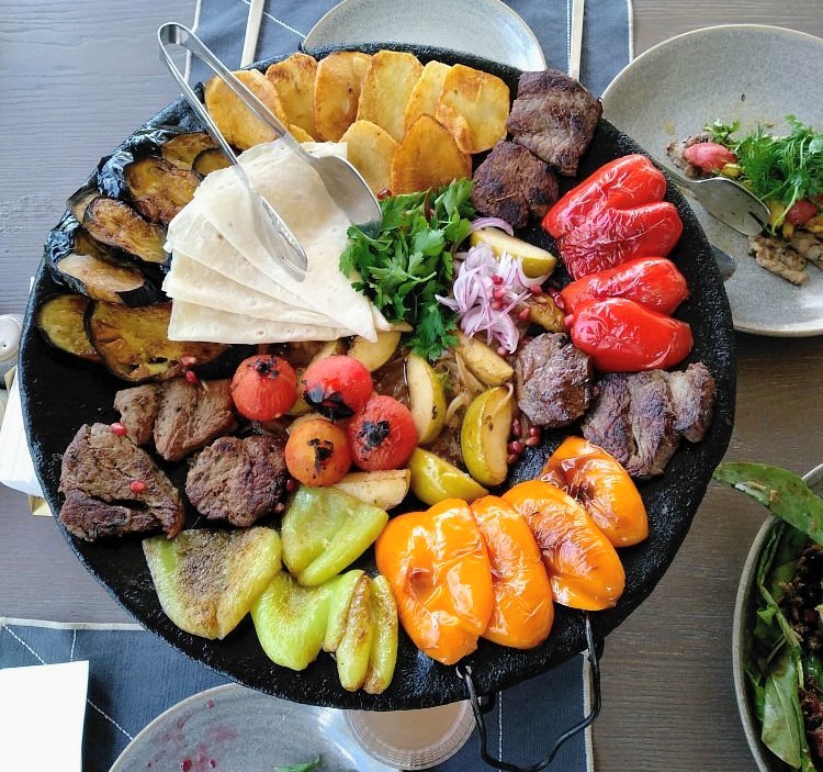 A cast-iron saj platter of grilled lamb, aubergine, sweet peppers, potatoes and lavash, served family style