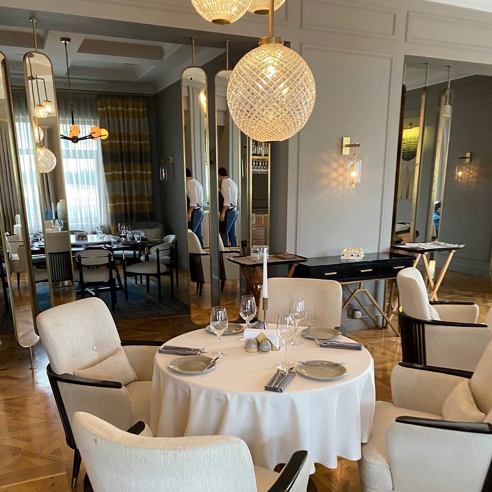 A bright dining room at Chayki in Baku with brass-framed mirrors, crystal globe pendants and a dressed round table