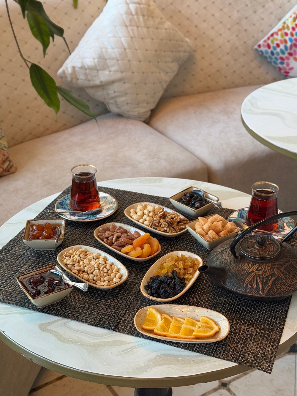 An Azerbaijani tea table with two glasses of tea, a cast-iron teapot, preserves, almonds, walnuts, dried fruit and orange slices