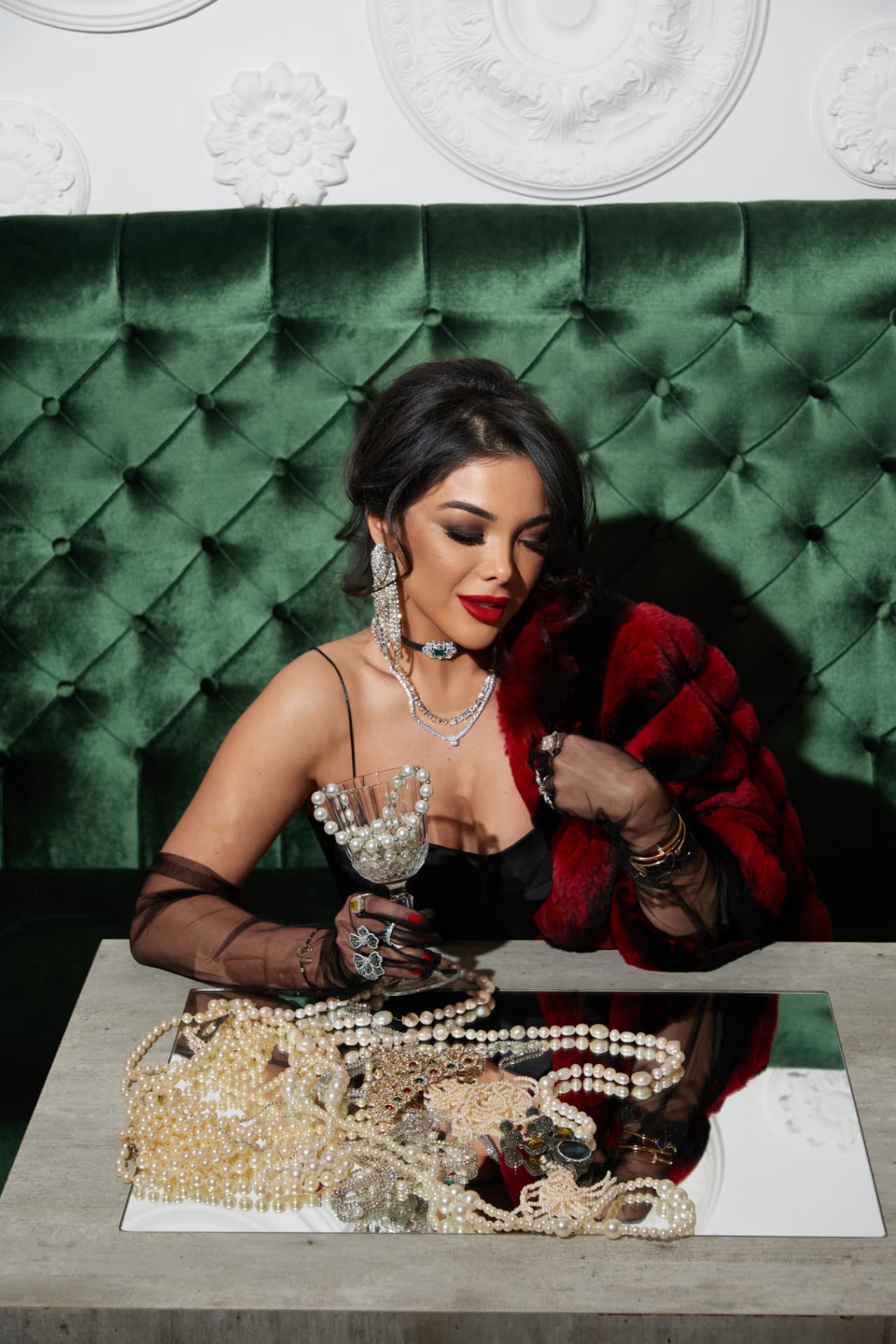 Kamila Verdiyeva seated at a table in a green velvet salon