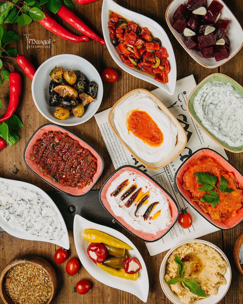 Cold starters of olives, roasted peppers, herbed yoghurt and hummus on a wooden table at Mangal Steak House in Baku