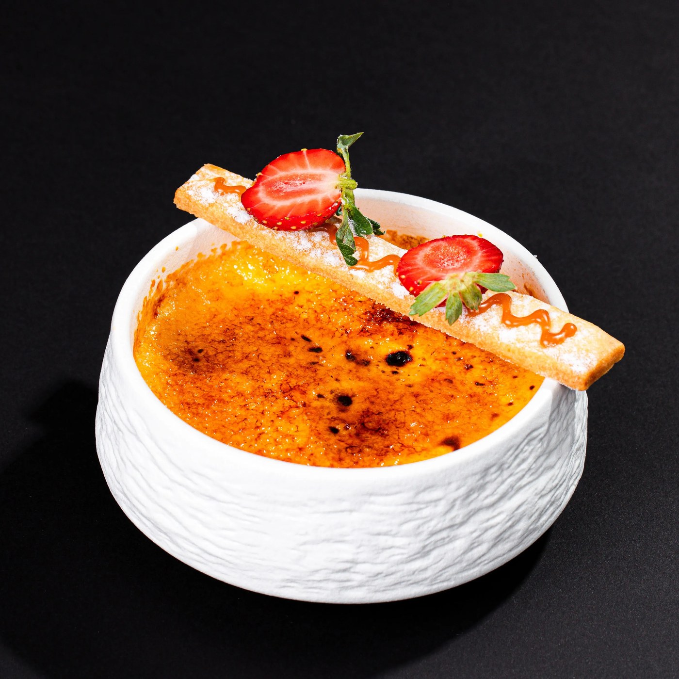A caramelised custard dessert with strawberries and a wafer