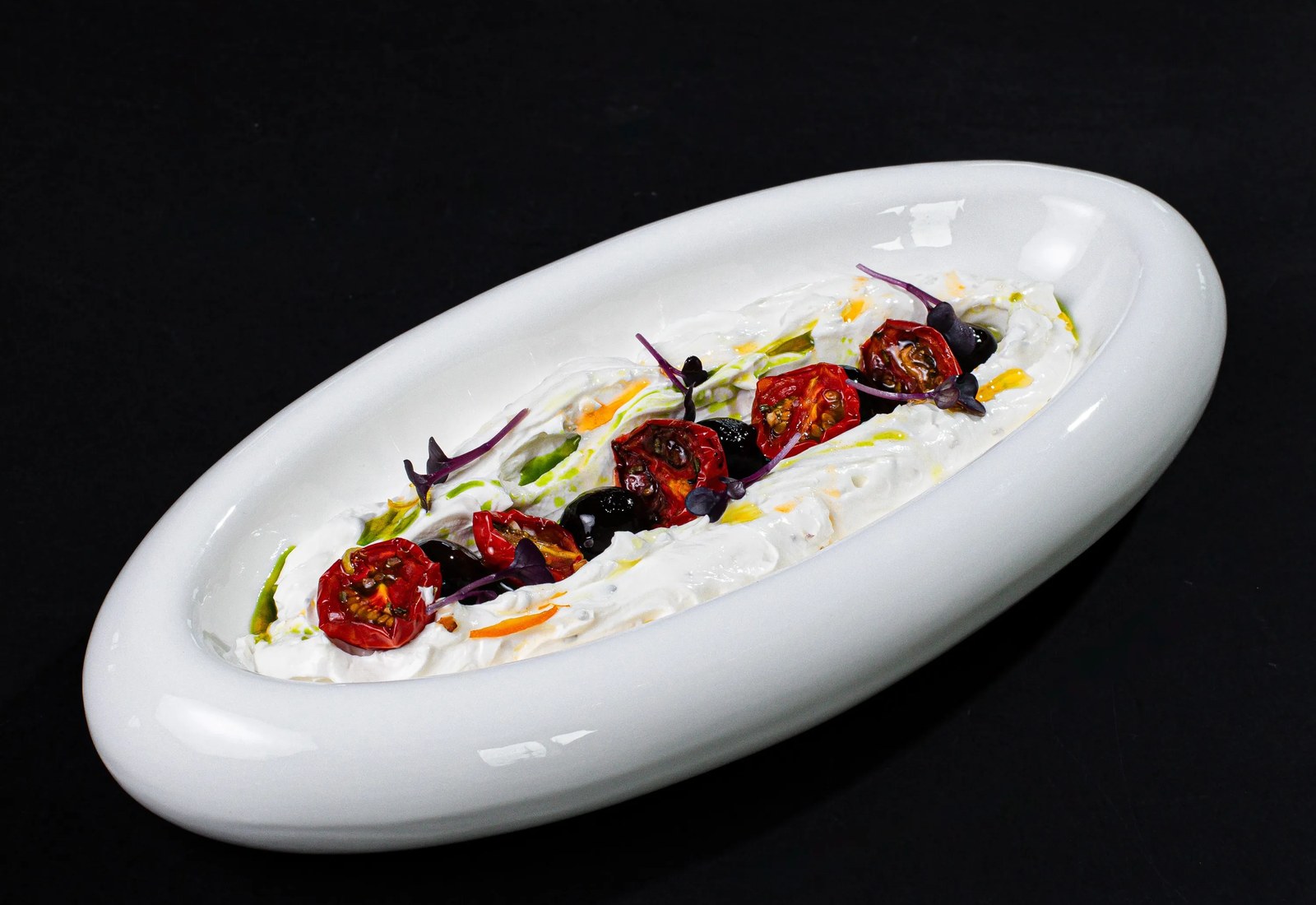 A long porcelain plate of mezze finished with confit tomatoes and olives